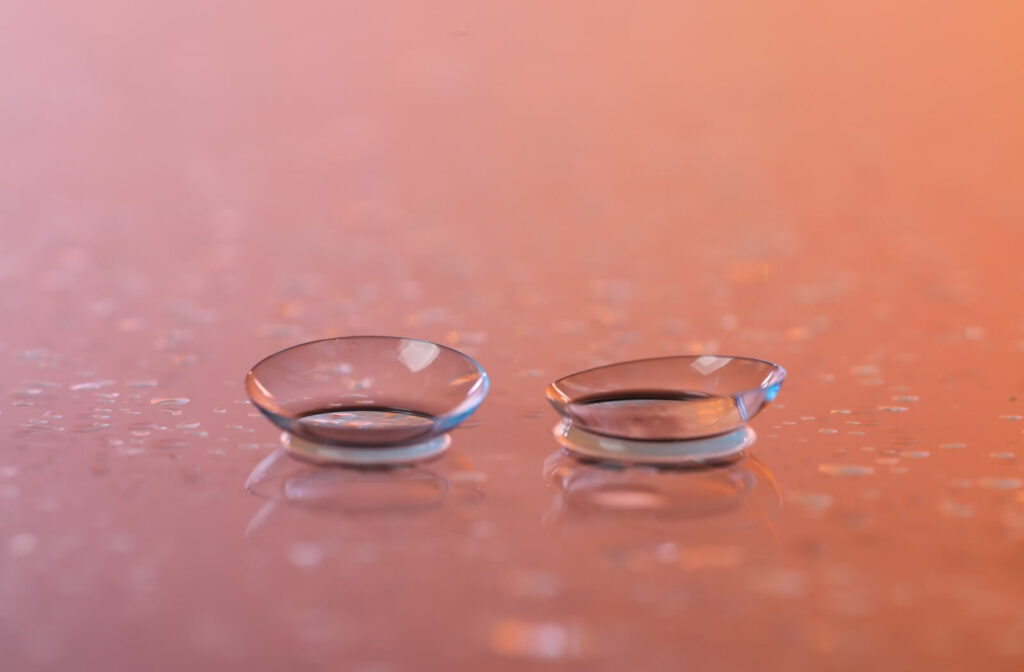 A pair of contact lenses sits on top of a table covered in water droplets. The light casts a faint orange glow over the table.