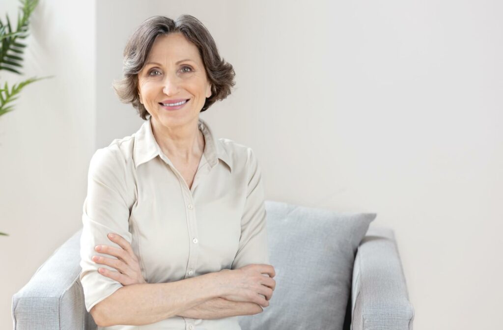 A senior woman with short brown hair sitting on a sofa and smiling, illustrating life after intraocular lens surgery.