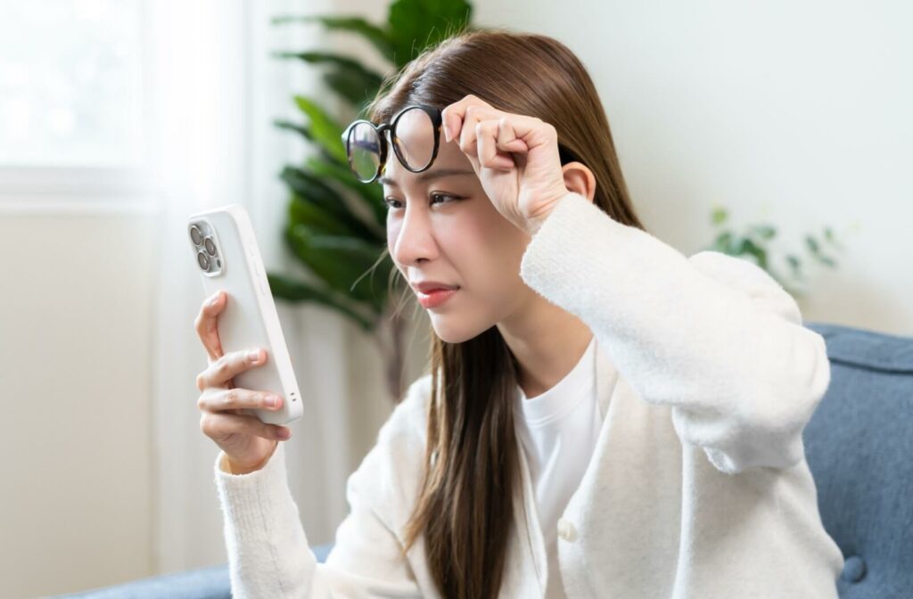 Squinting at a smartphone screen while lifting eyeglasses to see clearly.
