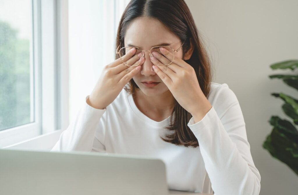 An adult rubbing their eyes while sitting at a laptop.